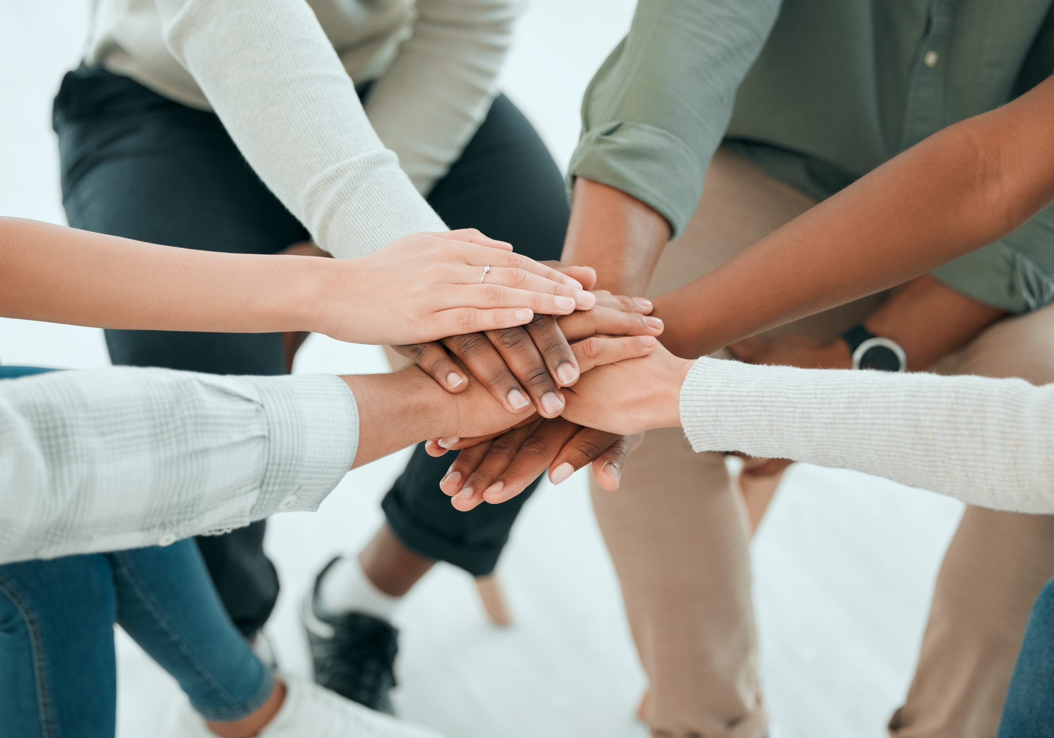 Multicultural people gathered in a circle with their hands stacked together showing unity.